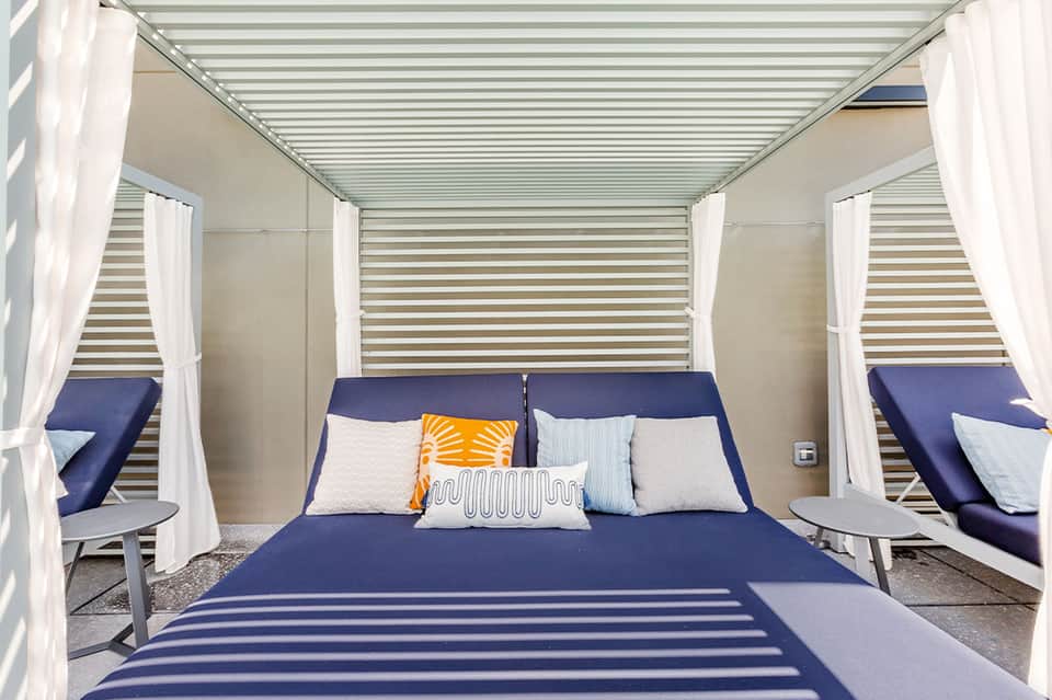 Modern canopy bed with navy bedding, white curtains, and striped ceiling inside resort cabana