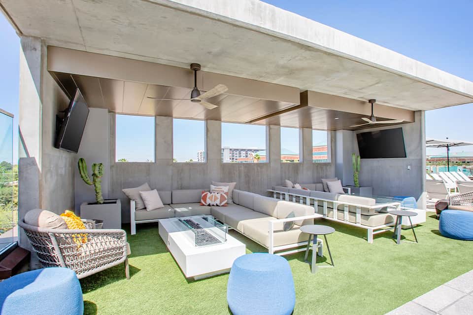 Rooftop lounge area with sectional seating, fire pit, ceiling fans, and city skyline views