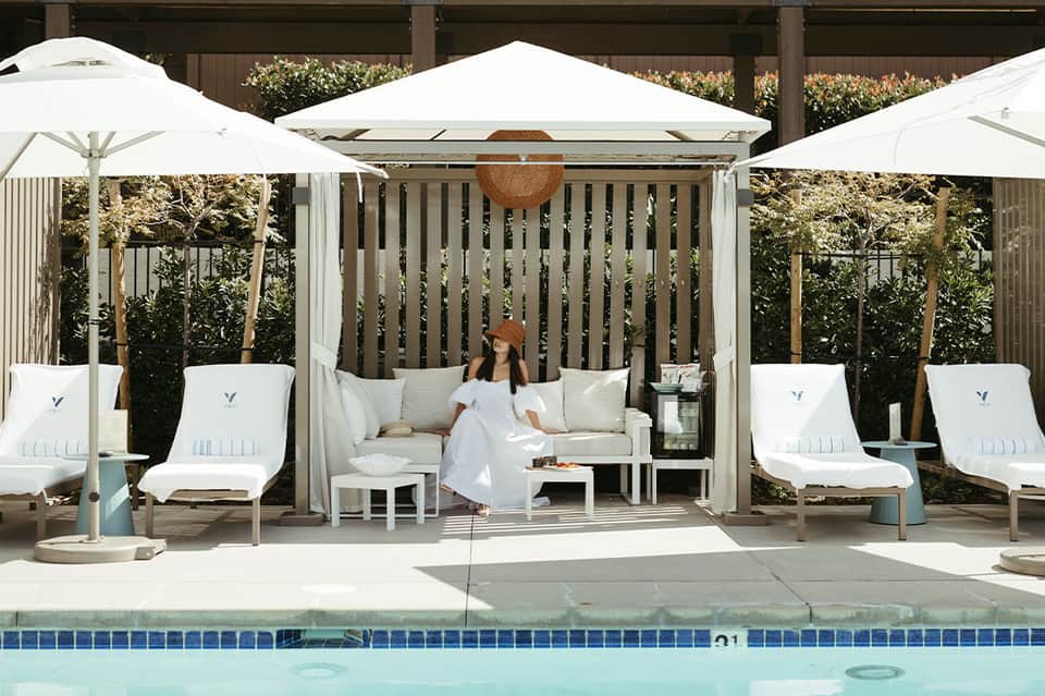 Woman in white dress sitting in cabana with white umbrellas by pool