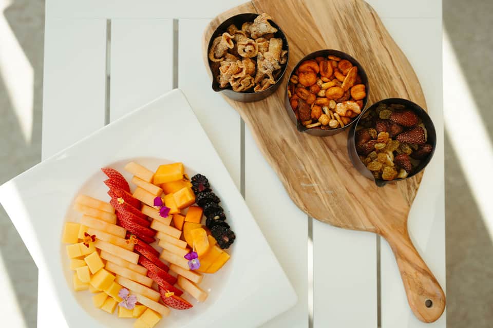 Fruit and snack board with colorful arranged cheese, strawberries, and various nuts in bowls