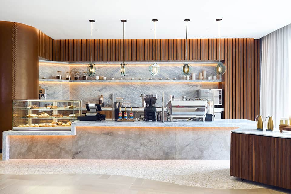 Modern hotel coffee bar with marble counter, wood paneling, and pendant lighting