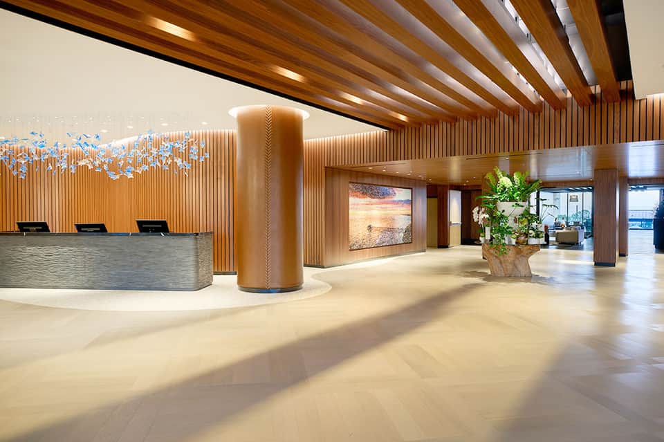 Contemporary hotel lobby with wooden slat walls, stone column, and ocean view artwork