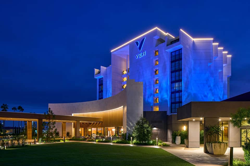 Modern hotel building illuminated in blue at dusk with neon outline trim and palm trees