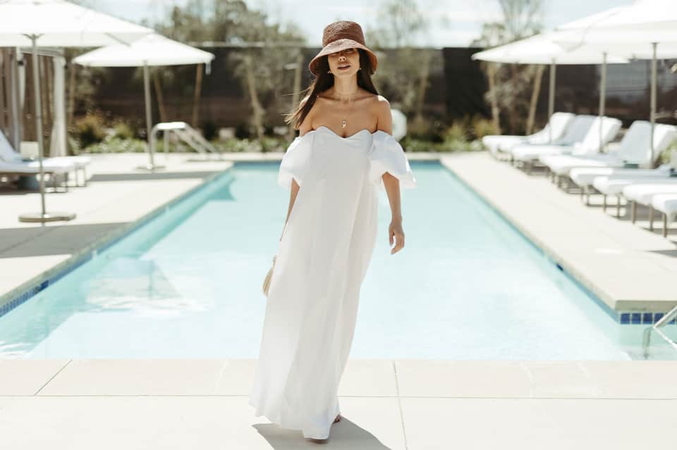 Woman in white dress at luxury resort pool surrounded by lounge chairs and white umbrellas