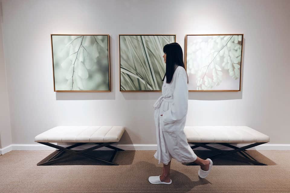 Spa corridor with woman viewing three framed botanical prints above white upholstered benches
