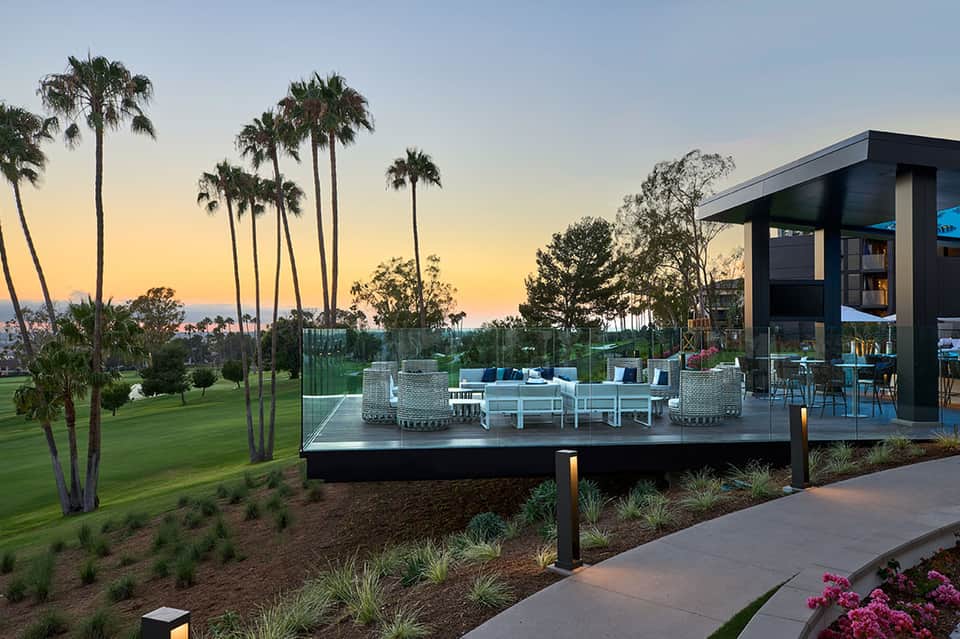 Modern pavilion overlooking golf course at dusk with palm trees, seating area, and grassy landscape