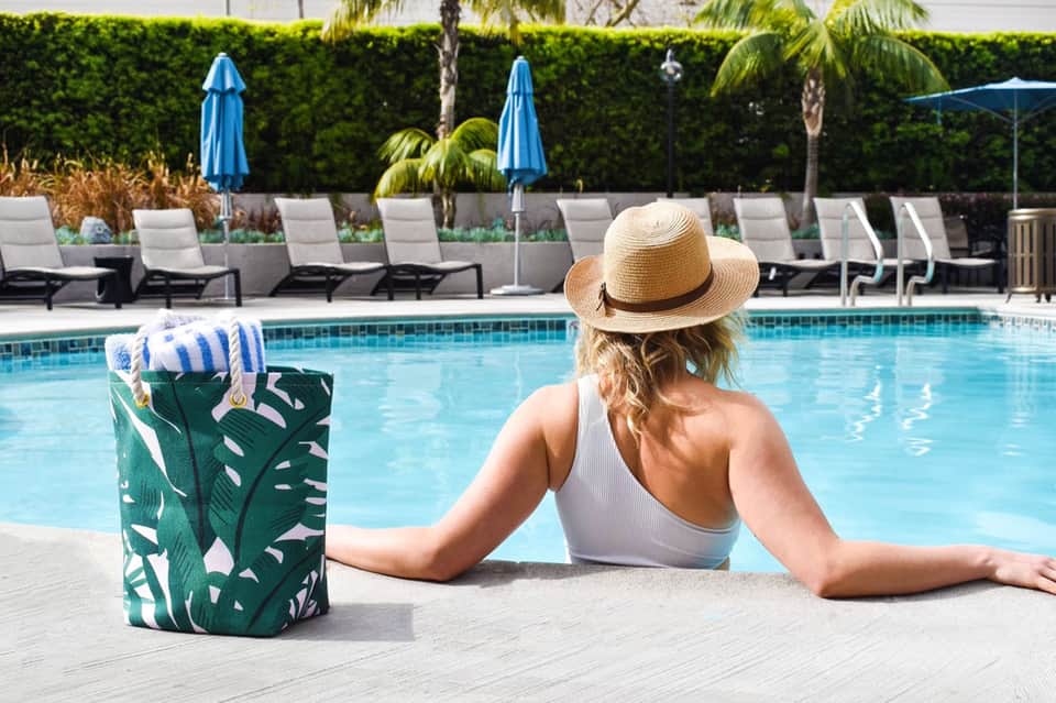 Woman relaxing in pool wearing sun hat with lounge chairs and umbrellas in background