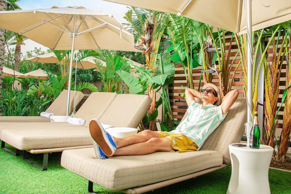 Man relaxing on sun lounger under umbrella in tropical garden setting