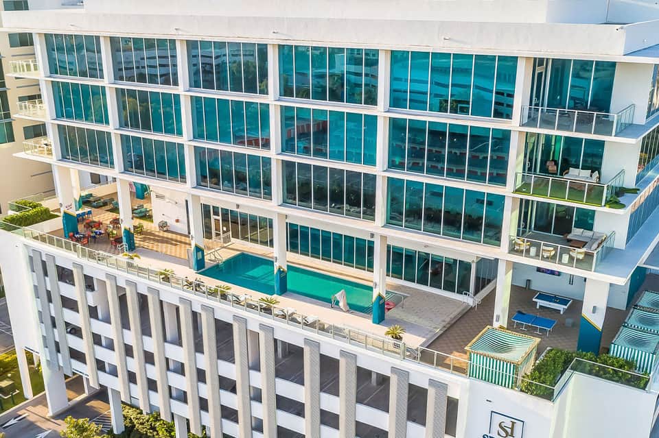 Modern oceanfront resort building with teal-green windows, white frame, ground-level pool, and multiple balconies