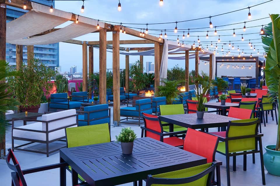 Colorful rooftop lounge area with wooden pergolas, string lights, and vibrant seating