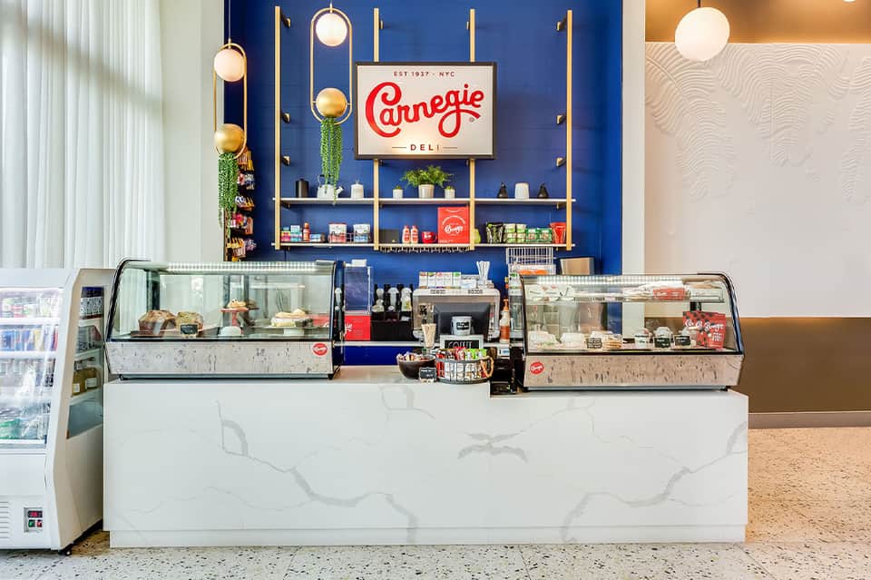 Modern deli counter with blue wall, Carnegie Deli signage, glass display cases, and hanging pendant lights