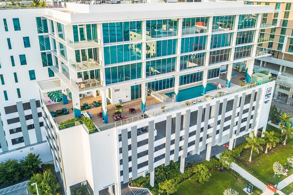 Modern resort building with large turquoise pool, lounge seating, and contemporary white architecture