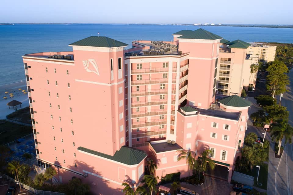 Aerial view of pink resort buildings with green roofs overlooking blue bay and distant bridge