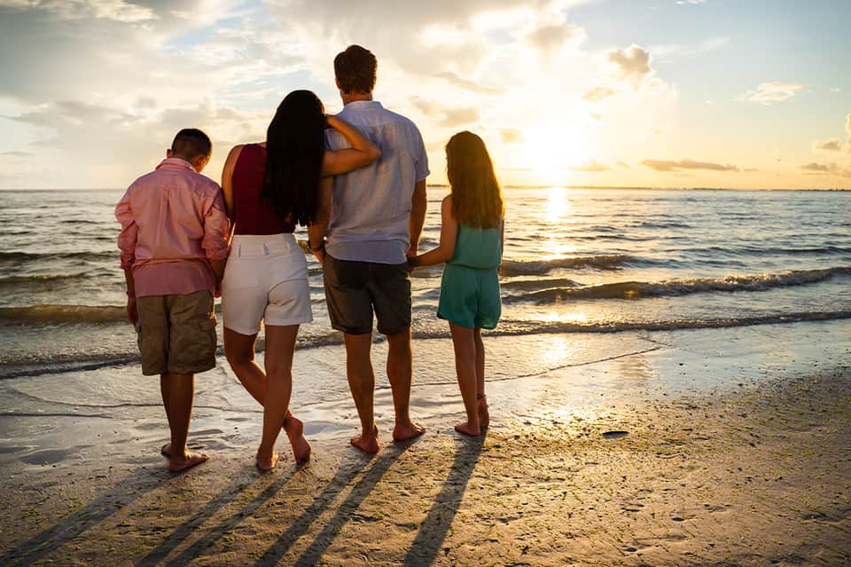 Family of four standing at beach shoreline at golden sunset