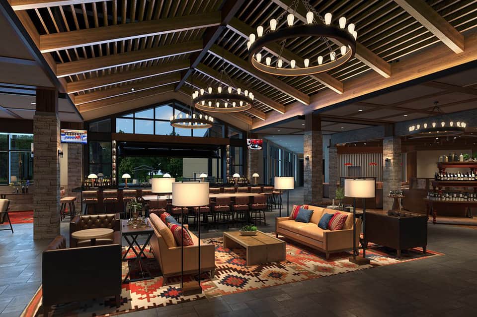 Upscale hotel lobby with wooden ceiling beams, circular chandeliers, tan sofas, and contemporary furnishings
