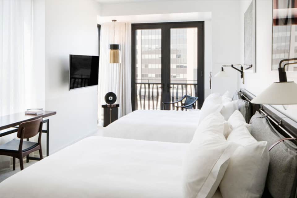 Contemporary hotel room with two beds, flat-screen TV, balcony doors, and city views