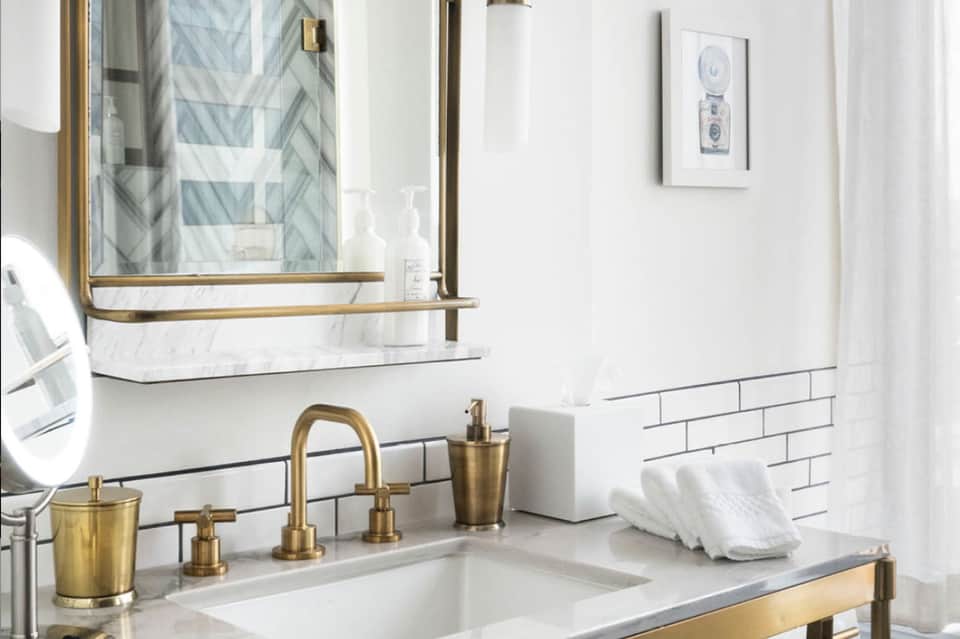 Luxury bathroom vanity with white marble, brass fixtures, subway tile backsplash, and framed artwork