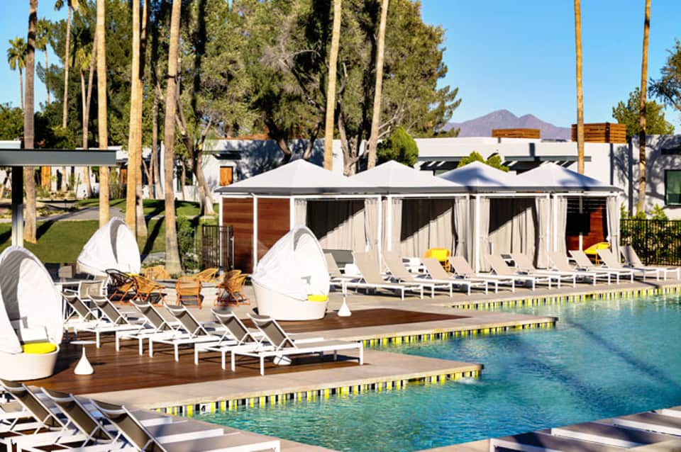 Luxury resort poolside with white cabanas, loungers, and tall palm trees lining the deck