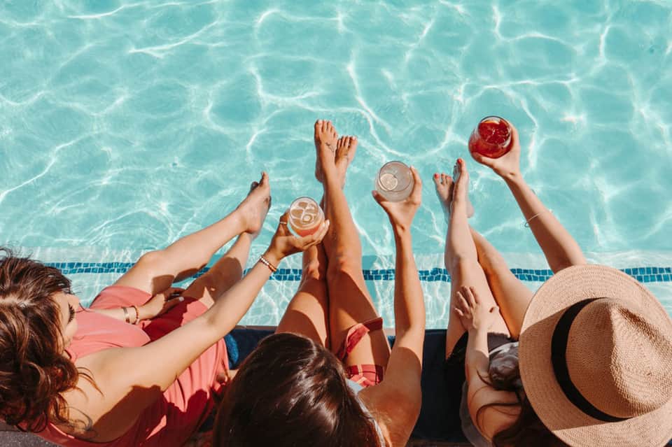 Group of friends toasting with colorful cocktails while relaxing poolside on a sunny day