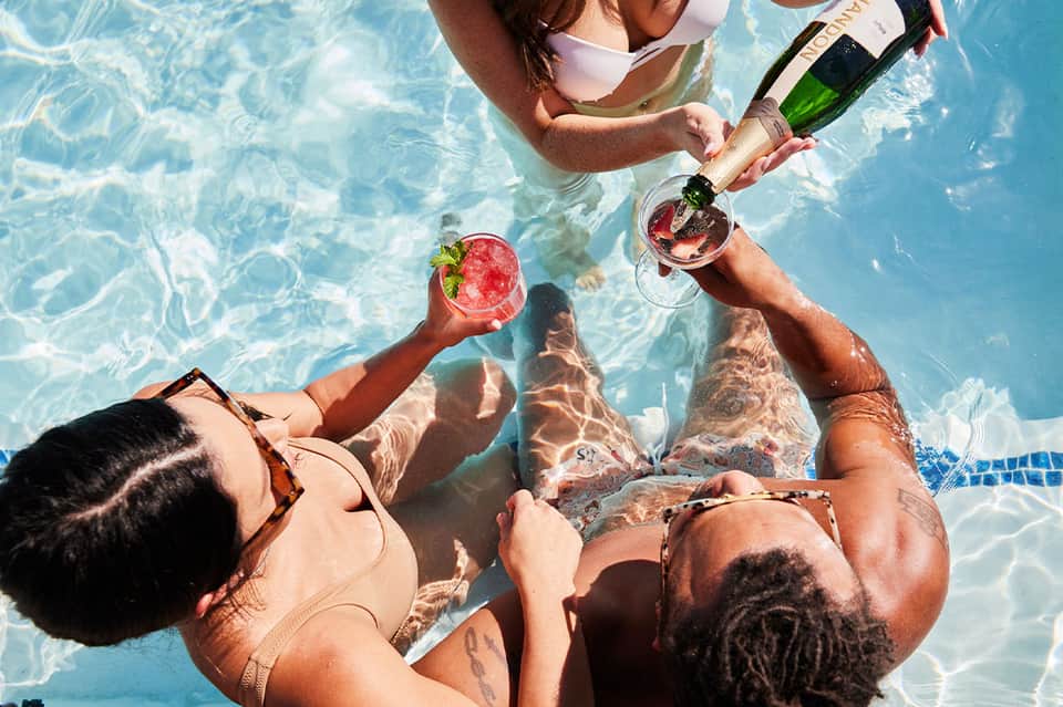 Overhead view of people toasting with drinks in swimming pool on sunny day