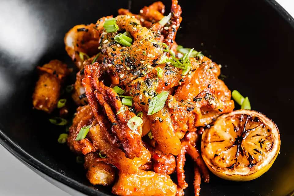 Gourmet plated chicken dish with Asian glaze, charred lemon, and green onion garnish on black plate