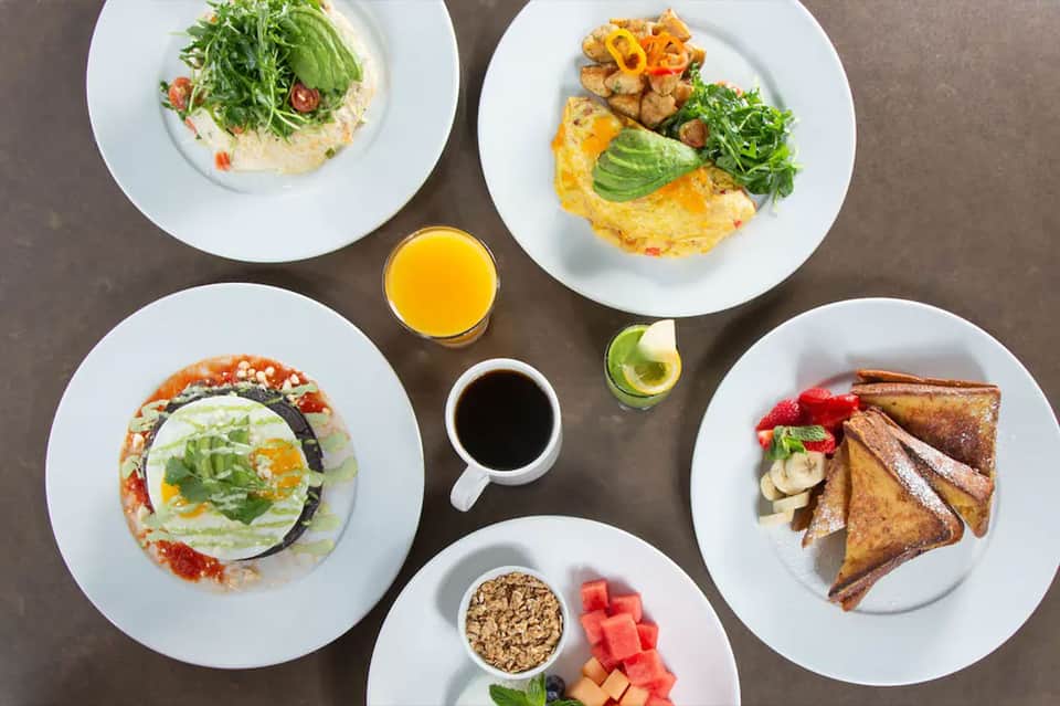 Colorful gourmet breakfast dishes including omelets, toast, salad, juice, and coffee overhead