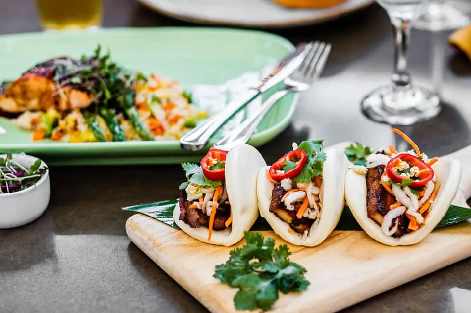 Three Asian fusion bao buns with meat and vegetables on wooden board