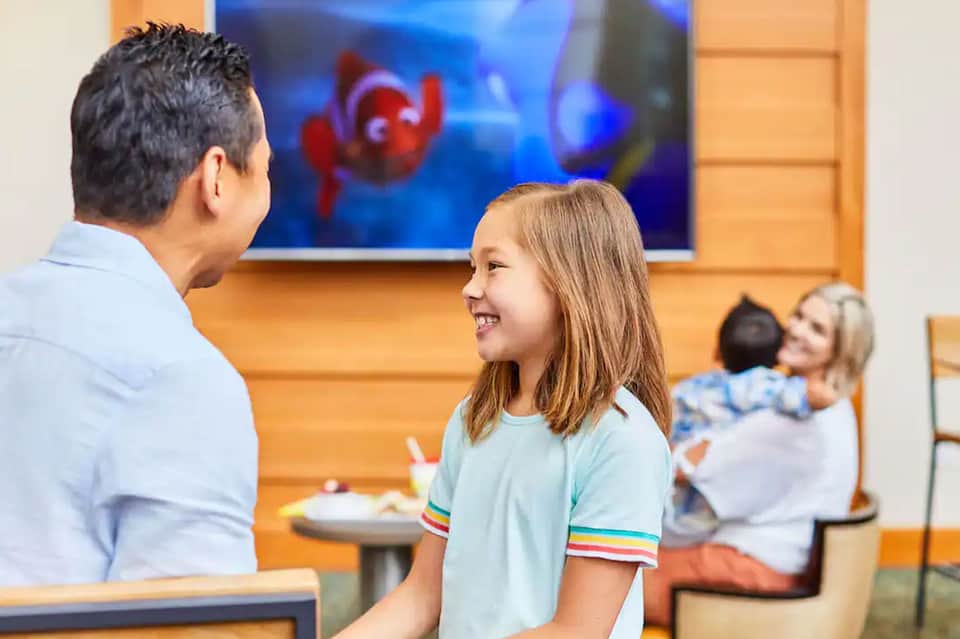 Family enjoying meal at casual resort restaurant with father and daughter in foreground, warm orange walls