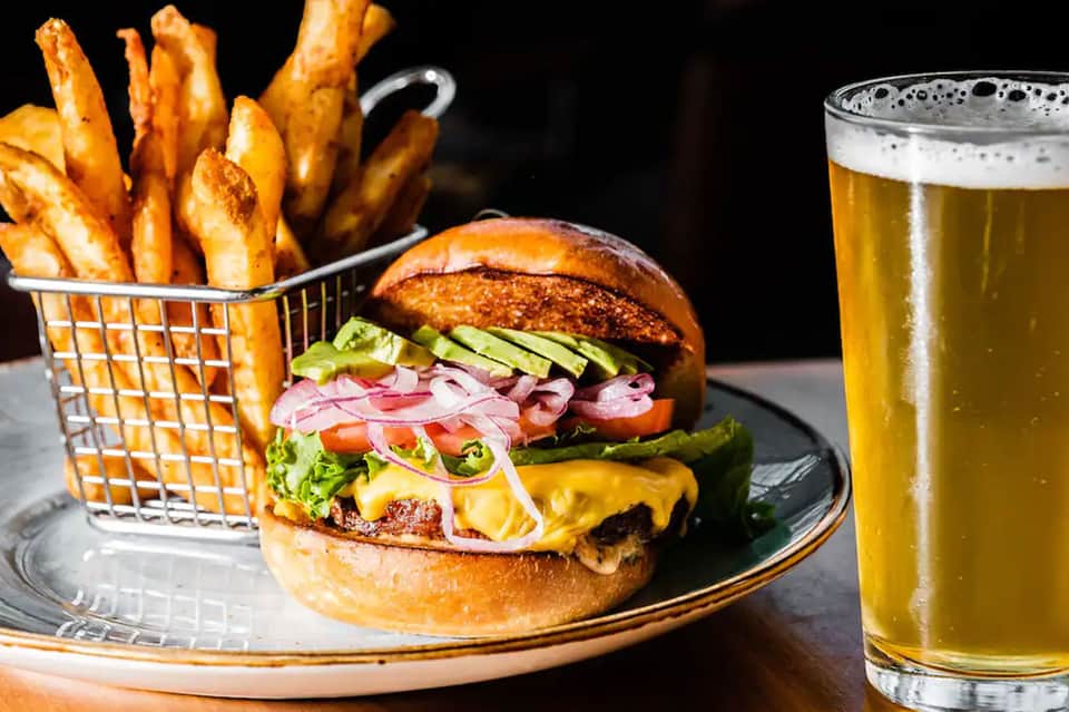 Gourmet burger with fries and cold beer on dark plate against black background