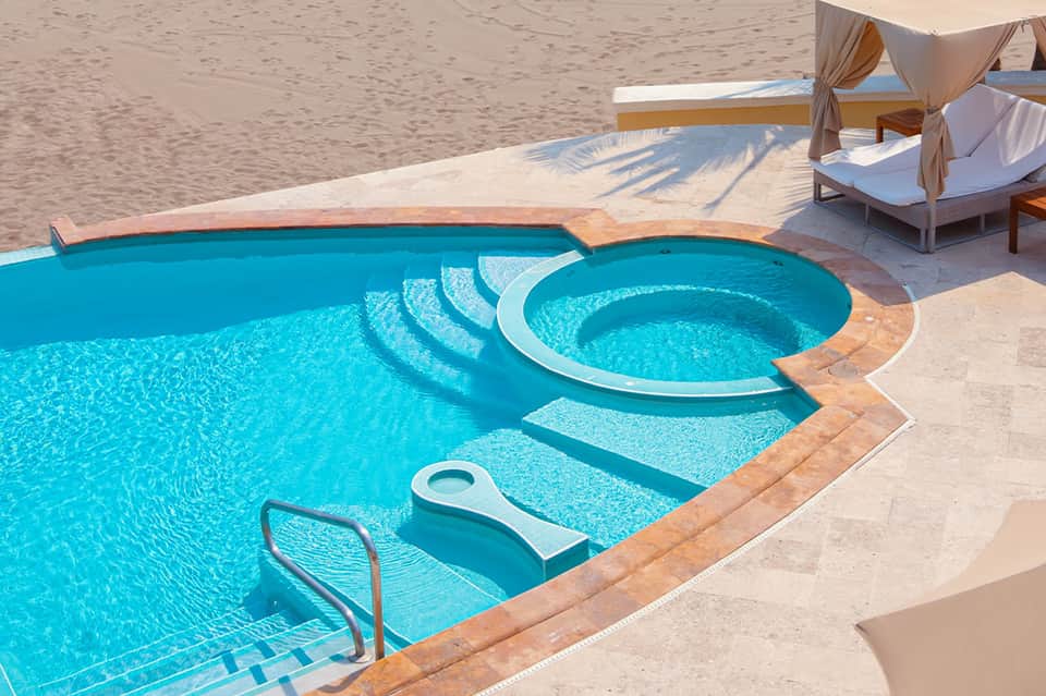Luxury beachfront pool with spa hot tub, cabanas with white drapes, and sandy beach access