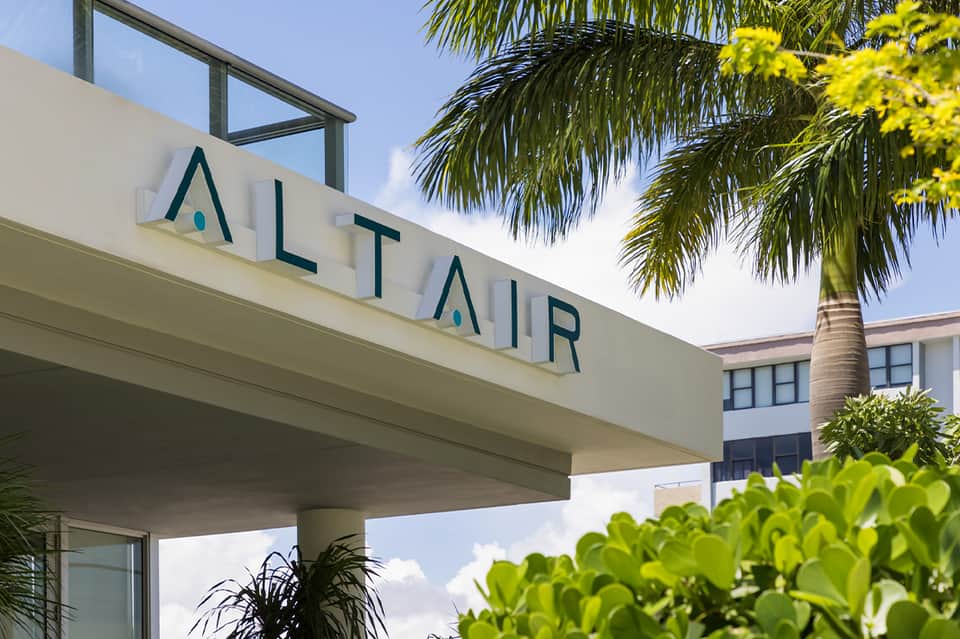 Upscale resort sign reading ALTAR with palm tree and modern white architecture against blue sky