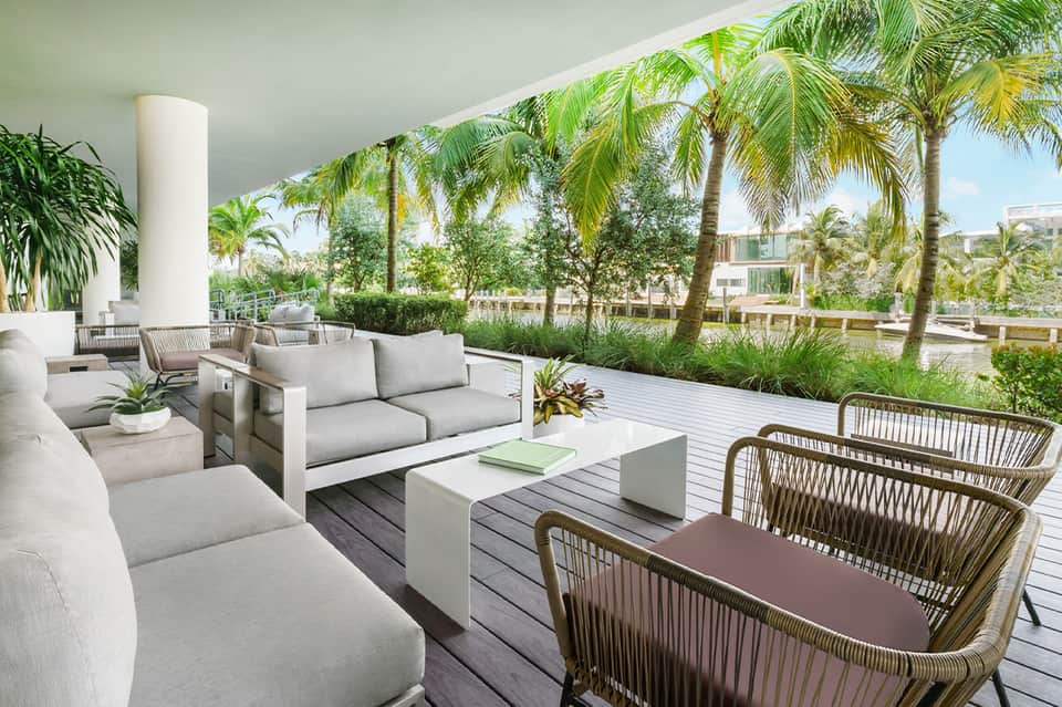 Elevated terrace with contemporary seating, white columns, palm trees, and garden views