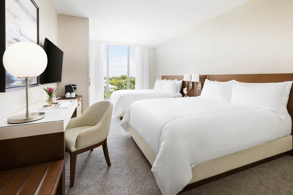 Modern hotel bedroom with two queen beds, white linens, wood headboard, and ocean view