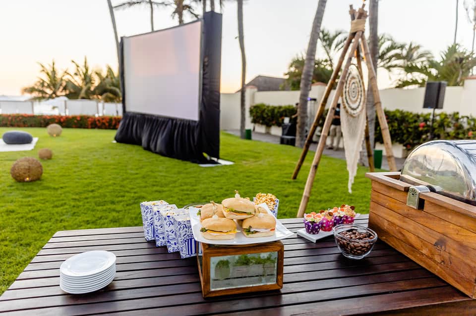 Outdoor lawn setup with food table, outdoor movie screen, and boho décor for evening event