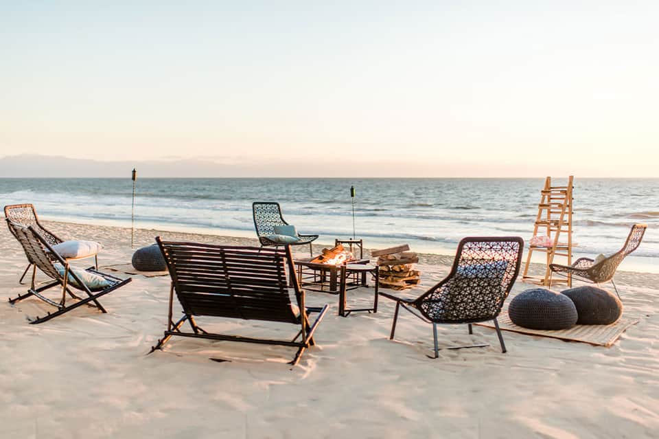 Modern beach furniture seating area on sand at dusk with ladder and decorative chairs by ocean
