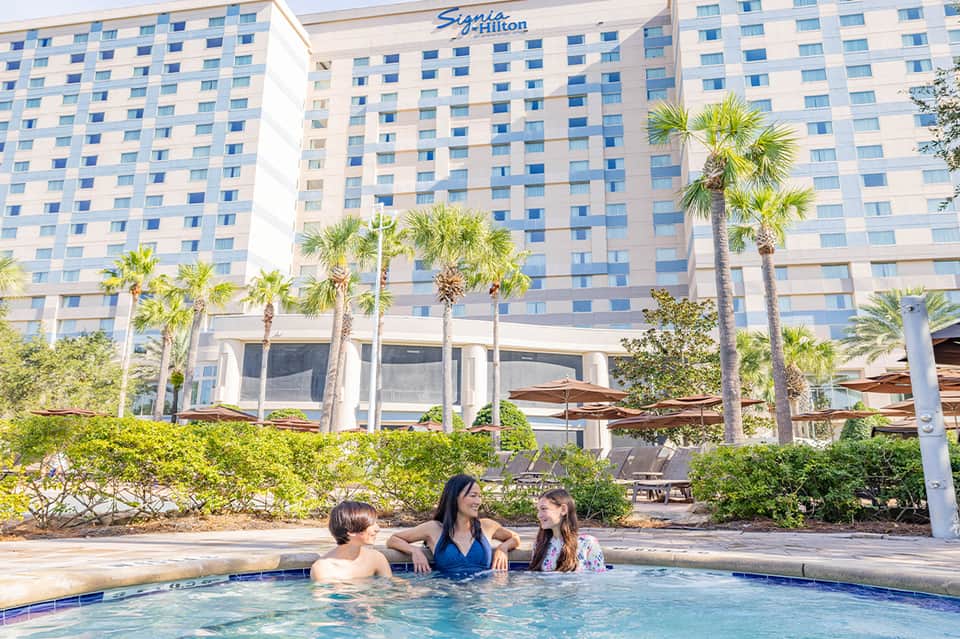 Signia Hilton hotel exterior with palm trees and guests enjoying outdoor pool area