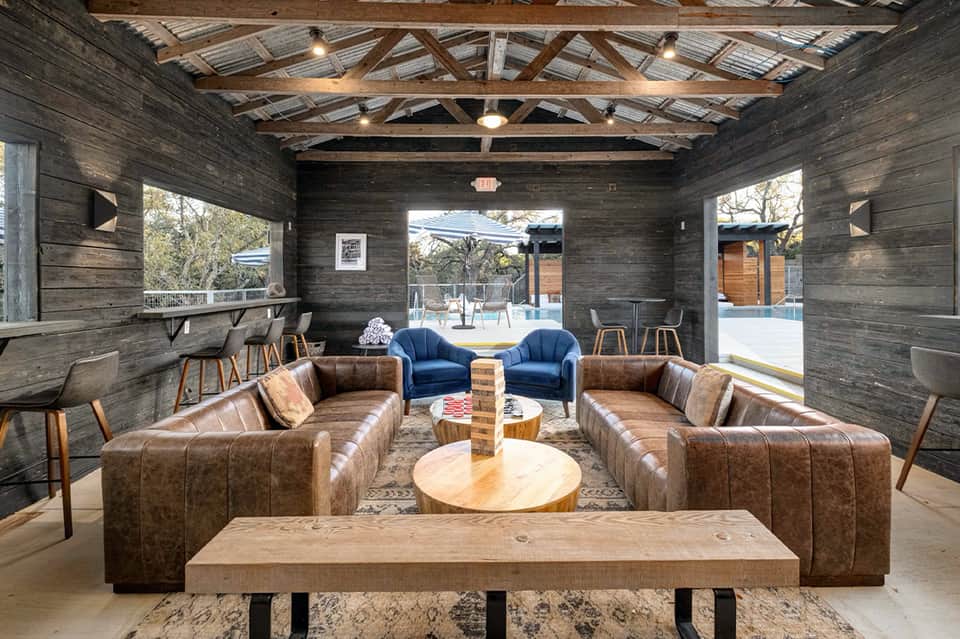 Modern lounge area with leather couches, wooden beams, blue accent chairs, and open patio