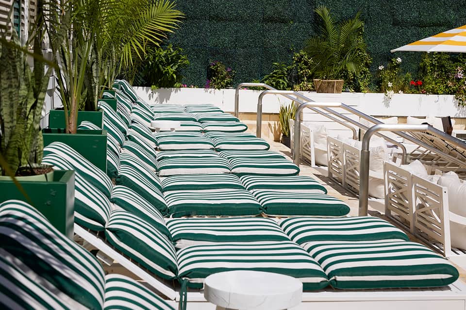 Row of green and white striped lounge chairs on sunny resort deck with potted plants and umbrella