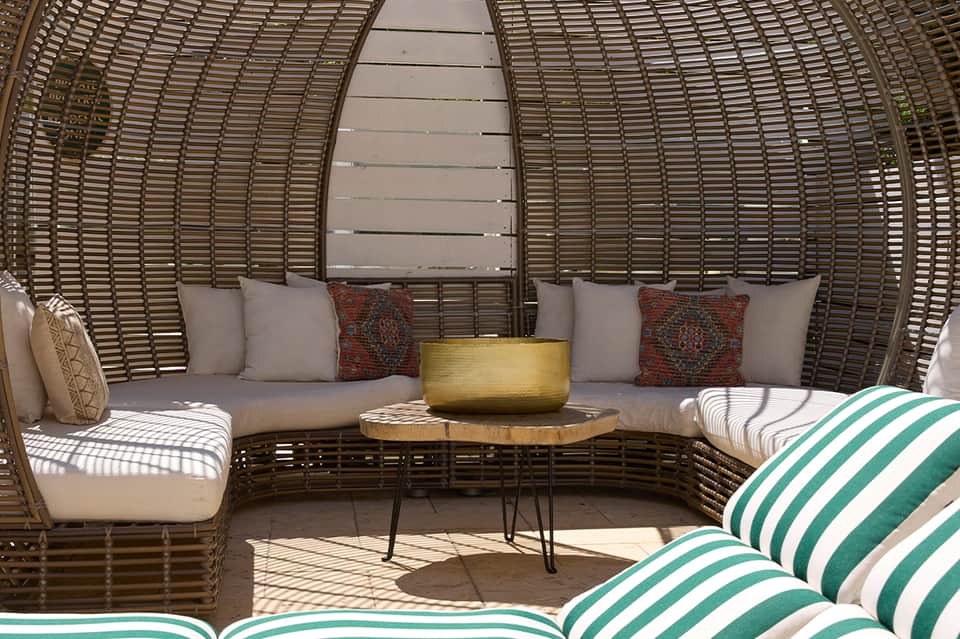 Curved woven wicker daybed seating area with beige cushions, pillows, and gold accent table