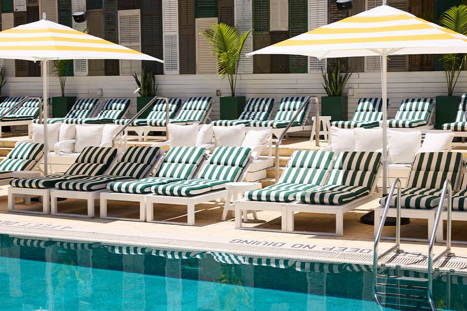 Resort poolside with green and white striped lounge chairs, yellow umbrellas, and cabanas