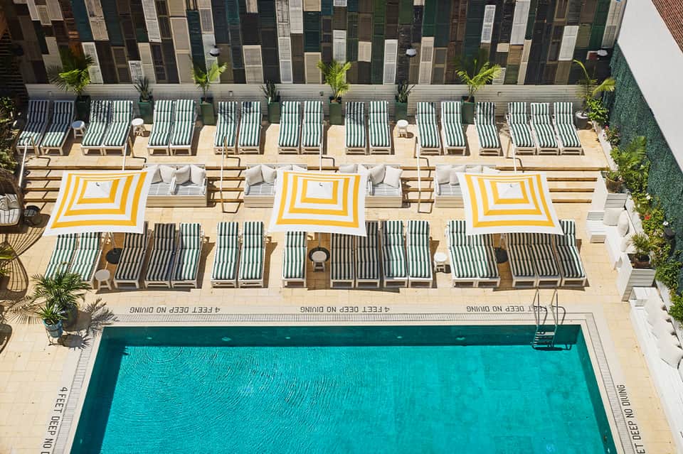 Aerial view of resort pool with striped lounge chairs, yellow umbrellas, and decorative fence