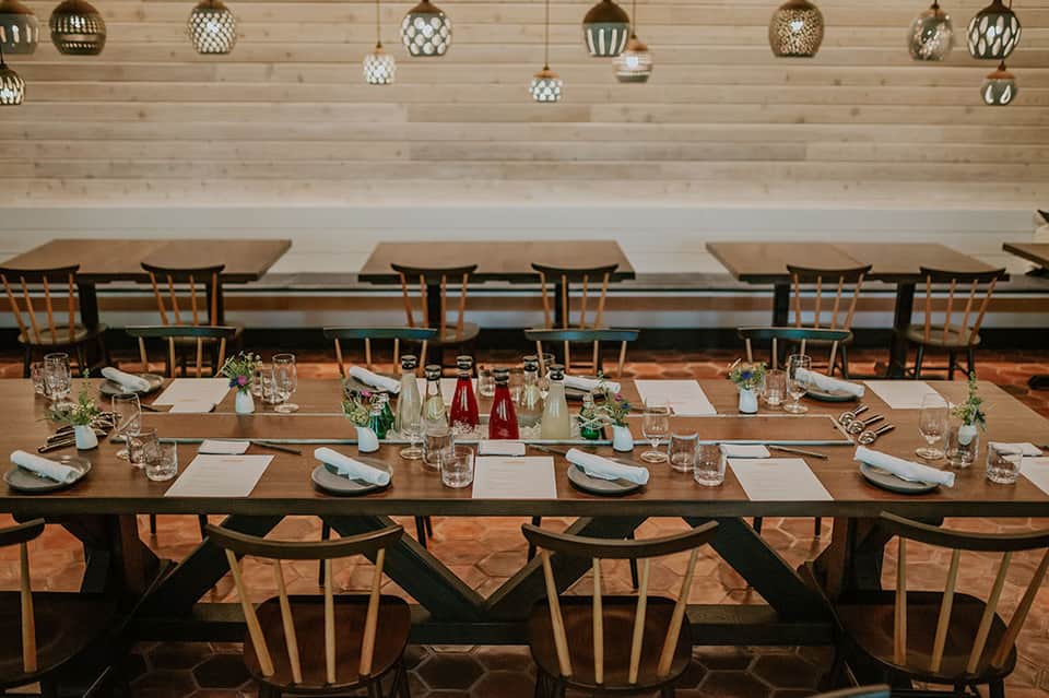 Elegant dining room with long wooden table, modern pendant lights, white brick wall, and mid-century modern chairs