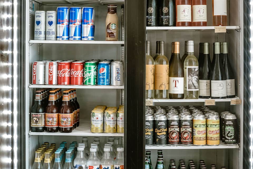 Refrigerated beverage display case stocked with soft drinks, beer, wine, and spirits