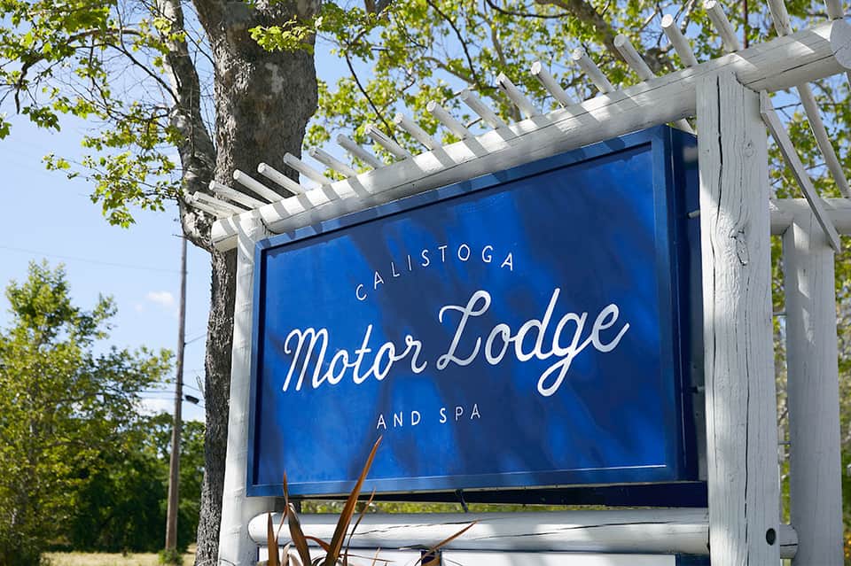 Blue motor lodge and spa sign on white pergola surrounded by trees