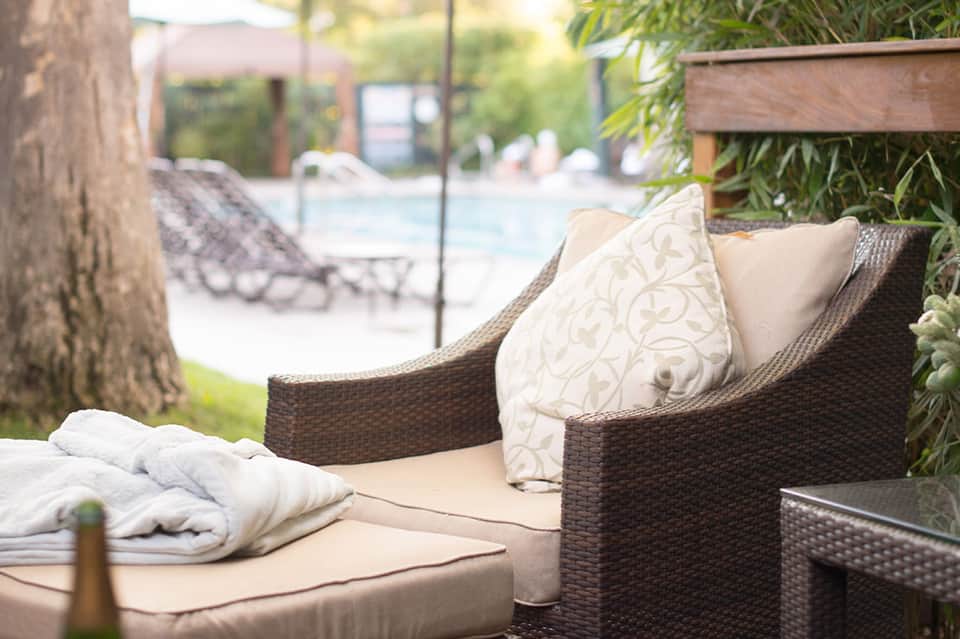 Woven lounge chair with cream cushions and decorative pillows near hotel pool and palm trees