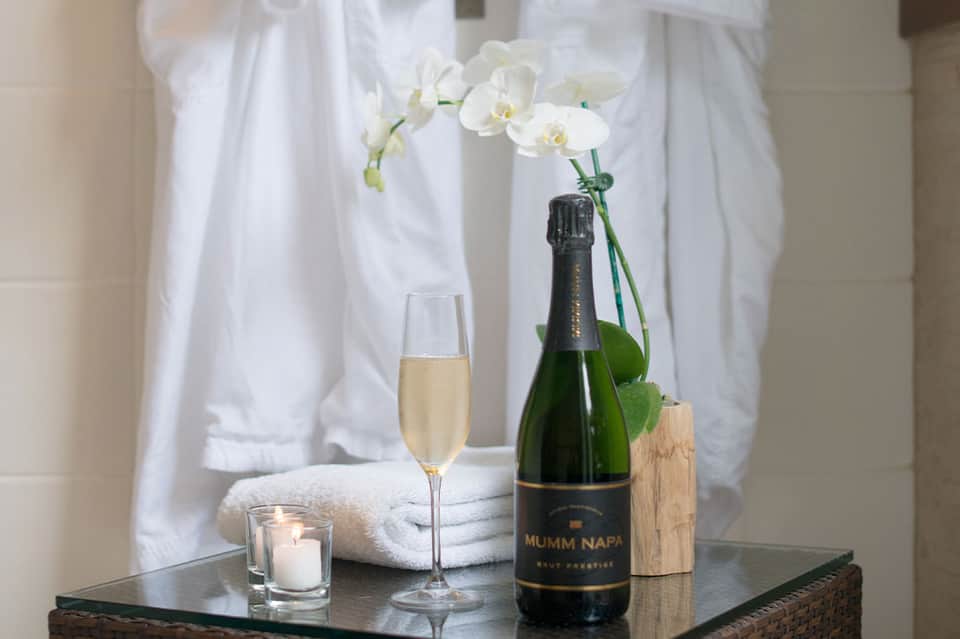 Luxury spa setting with champagne bottle, flute, white orchid, candle, and rolled towels