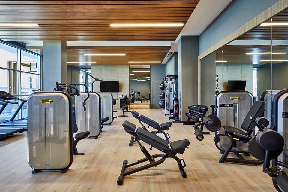 Modern fitness center with exercise equipment, wooden ceiling, and large windows