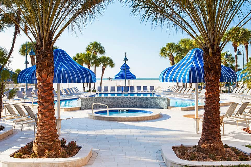 Elegant poolside cabanas with striped blue umbrellas and palm trees at resort
