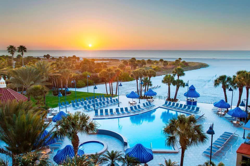 Aerial view of curved resort pool with blue umbrellas at sunset overlooking coastline