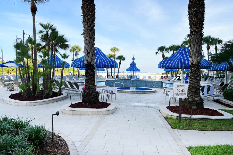 Resort pool area with blue umbrellas, palm trees, and tiered lounging spaces